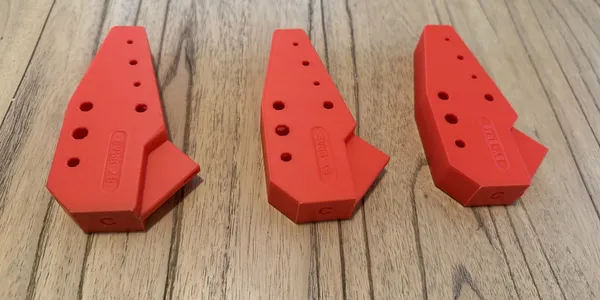 Three red 3D printed prototype brackets with drilled mounting holes