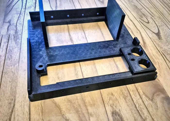 Black carbon-fibre 3D printed frame with mounting holes on a workbench