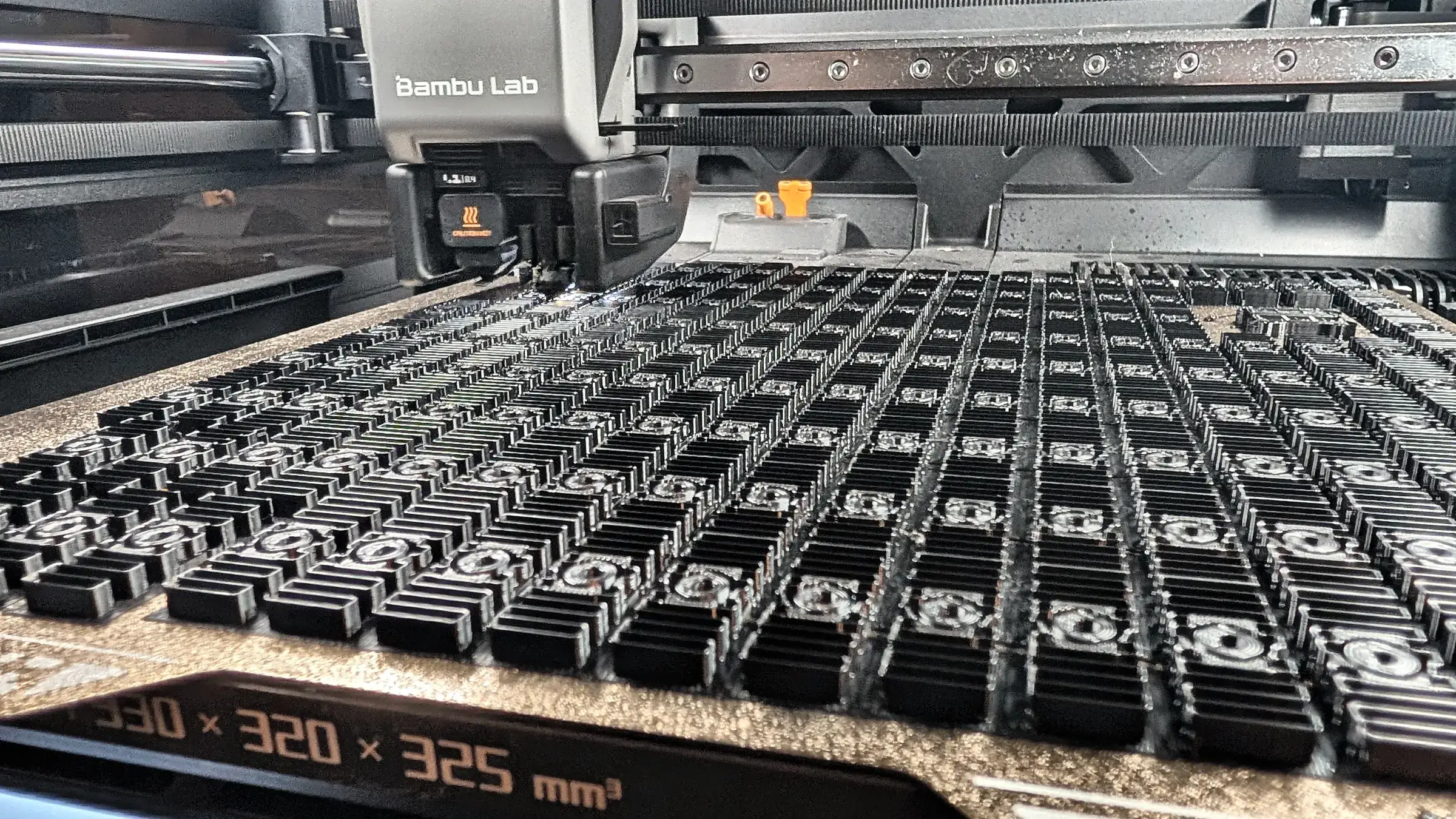 Hundreds of small black parts printed in one batch on a Bambu Lab printer in the Brisbane 3D Printing workshop